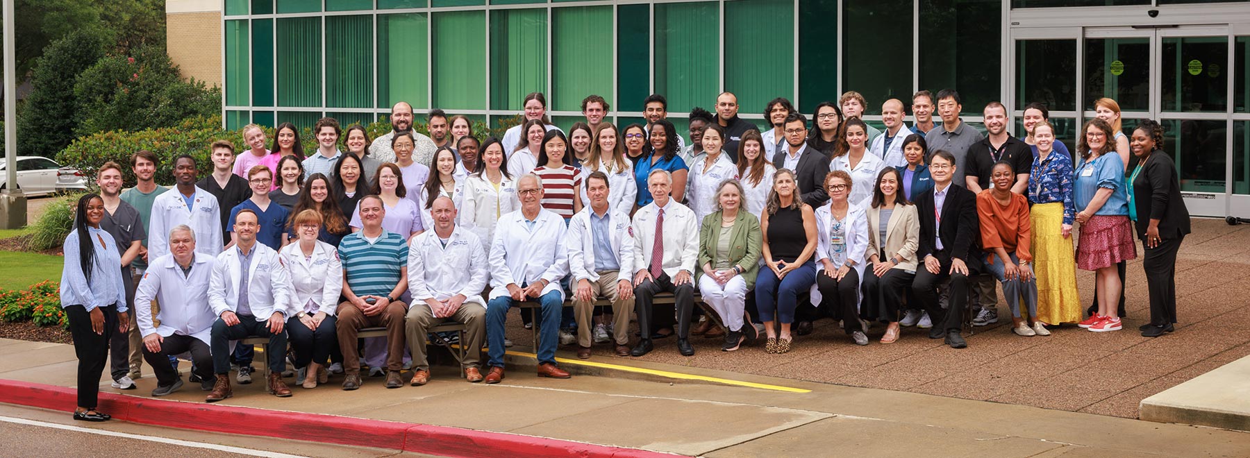 Group photo of department members in front of the John E. Hall Research Building. Dr. John Hall is seated in the center.
